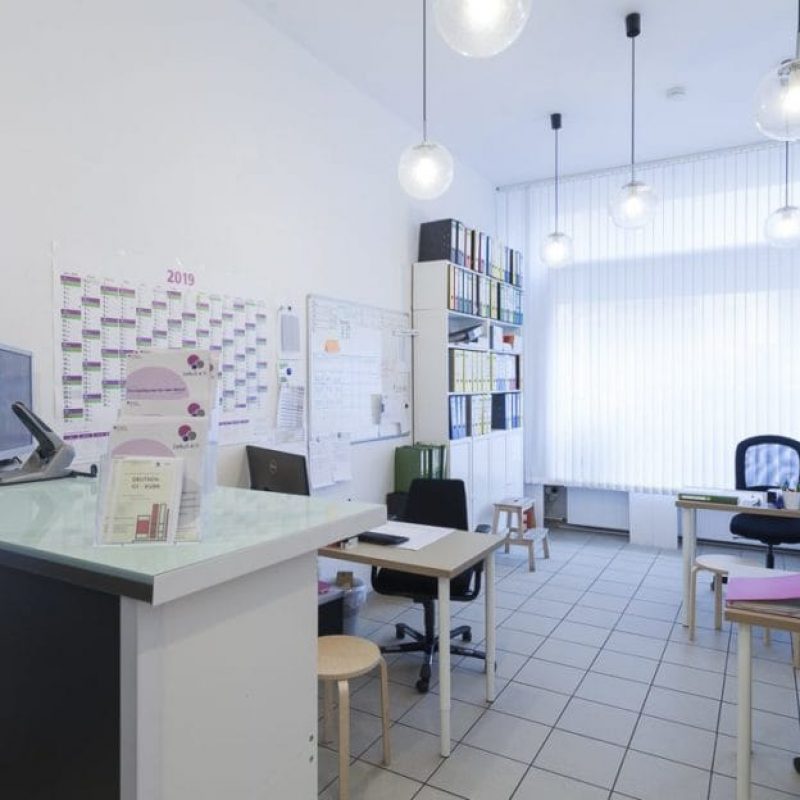 Helles, modernes Büro mit einem Empfangsbereich, mehreren Schreibtischen, organisierten Akten und großen Fenstern, die viel Tageslicht hereinlassen.